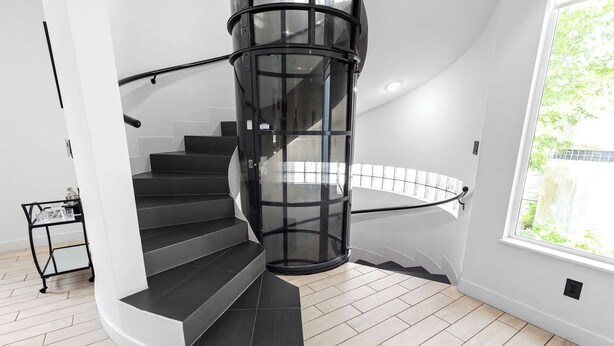 A modern spiral staircase with a glass railing, leading to a landing. - Montrose Rooftop Townhome | 3 Suites, Sleeps 8 (Houston)
