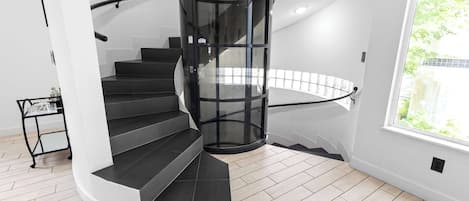 Un escalier en colimaçon moderne, doté d’une rampe en verre, menant à un palier.