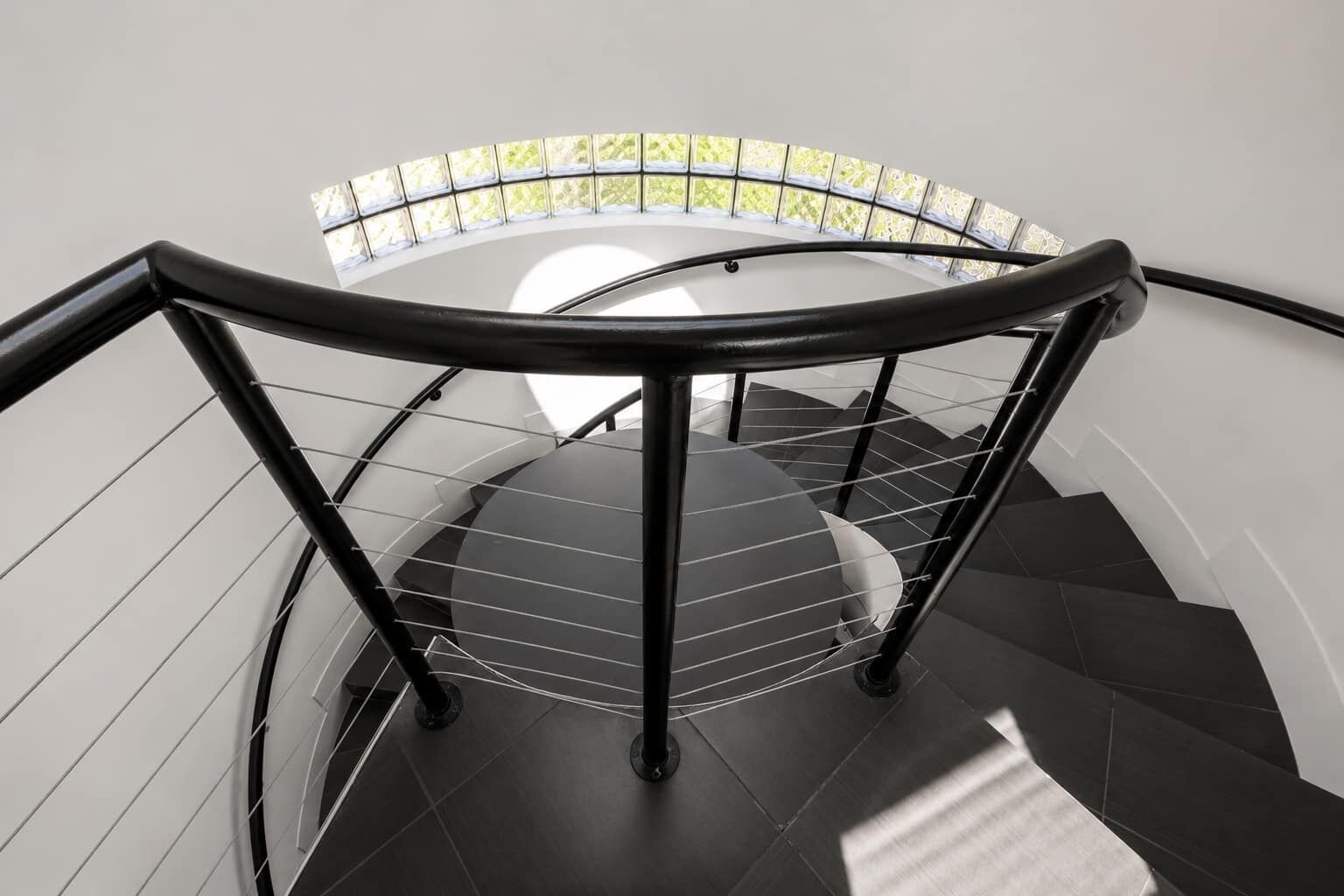 Escadaria em espiral com guarda-corpo de vidro e vista para o verde lá fora.