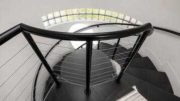 Escadaria em espiral com guarda-corpo de vidro e vista para o verde lá fora.