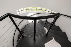 A spiral staircase with a glass railing and a view of greenery outside. - Montrose Rooftop Townhome | 3 Suites, Sleeps 8 (Houston)