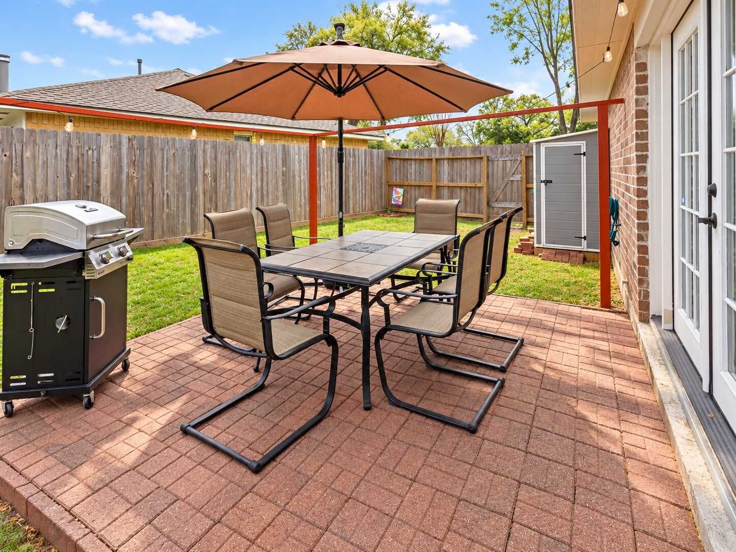 An outdoor patio with a grill, table, chairs, and an umbrella.