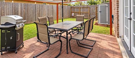 An outdoor patio with a grill, table, chairs, and an umbrella.