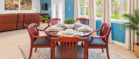 Un comedor con una mesa redonda preparada para cuatro personas, rodeada de sillas de madera con asientos acolchados.