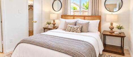 Quarto com uma cama grande, duas mesas de cabeceira com luminárias, uma janela com cortinas e uma porta que dá para um armário.