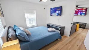 Ein Schlafzimmer mit Bett, Nachttisch, Lampe, Fernseher und Schreibtisch mit Stuhl.