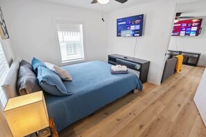 Ein Schlafzimmer mit Bett, Nachttisch, Lampe, Fernseher und Schreibtisch mit Stuhl.