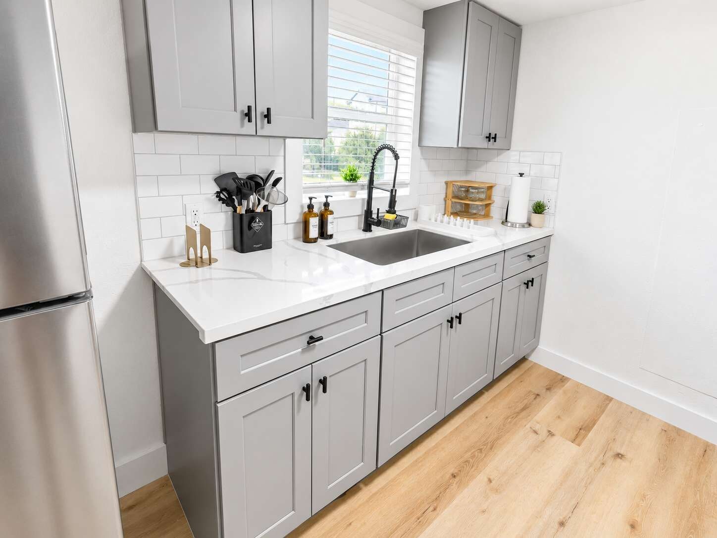 Una cocina moderna con armarios grises, una encimera blanca y un refrigerador de acero inoxidable.