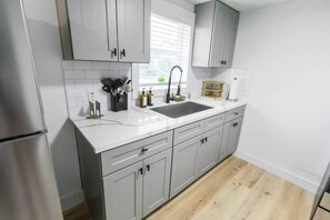 Eine moderne Küche mit weißen Schränken, einem Edelstahlkühlschrank, einer Spüle mit zwei Becken und einem Fenster mit Jalousien.