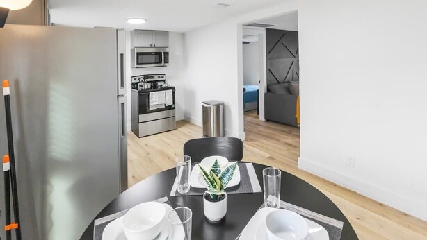 Eine moderne Küche mit Mikrowelle, Herd und Kühlschrank. Ein Esstisch mit Stühlen, ein Blumentopf und eine kleine Pflanze auf dem Tisch sind ebenfalls vorhanden.