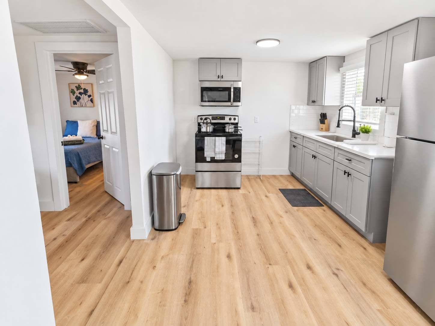 A modern kitchen with stainless steel appliances, grey cabinets, and a wooden floor.