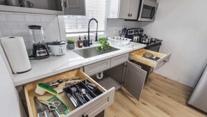 A modern kitchen with a white countertop, a built-in sink, a microwave, and a wooden drawer organizer. - 1BR Loft Near TSU + Med Center | Assigned Parking | Third Ward Houston 3 (Houston)