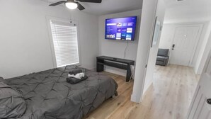 A bedroom with a bed, a desk, a TV, and a door leading to another room. - 1BR Loft Near TSU + Med Center | Assigned Parking | Third Ward Houston 3 (Houston)