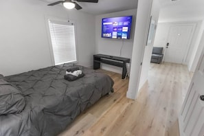 A bedroom with a bed, a desk, a TV, and a door leading to another room. - 1BR Loft Near TSU + Med Center | Assigned Parking | Third Ward Houston 3 (Houston)