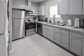 A modern kitchen with stainless steel appliances, grey cabinets, and a granite countertop. - 2BR Loft Near TSU + Med Center | In-Unit Laundry | Third Ward Houston 1 (Houston)