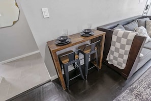 A dining area with a wooden table, two chairs, and a checkered throw on a sofa. - 2BR Loft Near TSU + Med Center | In-Unit Laundry | Third Ward Houston 1 (Houston)
