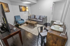 A modern living room with a sofa, armchair, coffee table, and a dining area with a table and chairs. - Historic 2BR Loft 2 I Med Center I NRG I Downtown (Houston)
