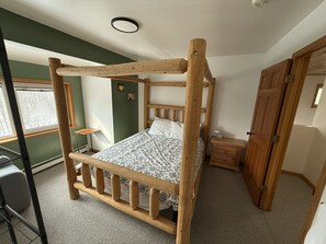 A wooden bunk bed with a headboard, a bedside table with a lamp, a window with a view, and a door.