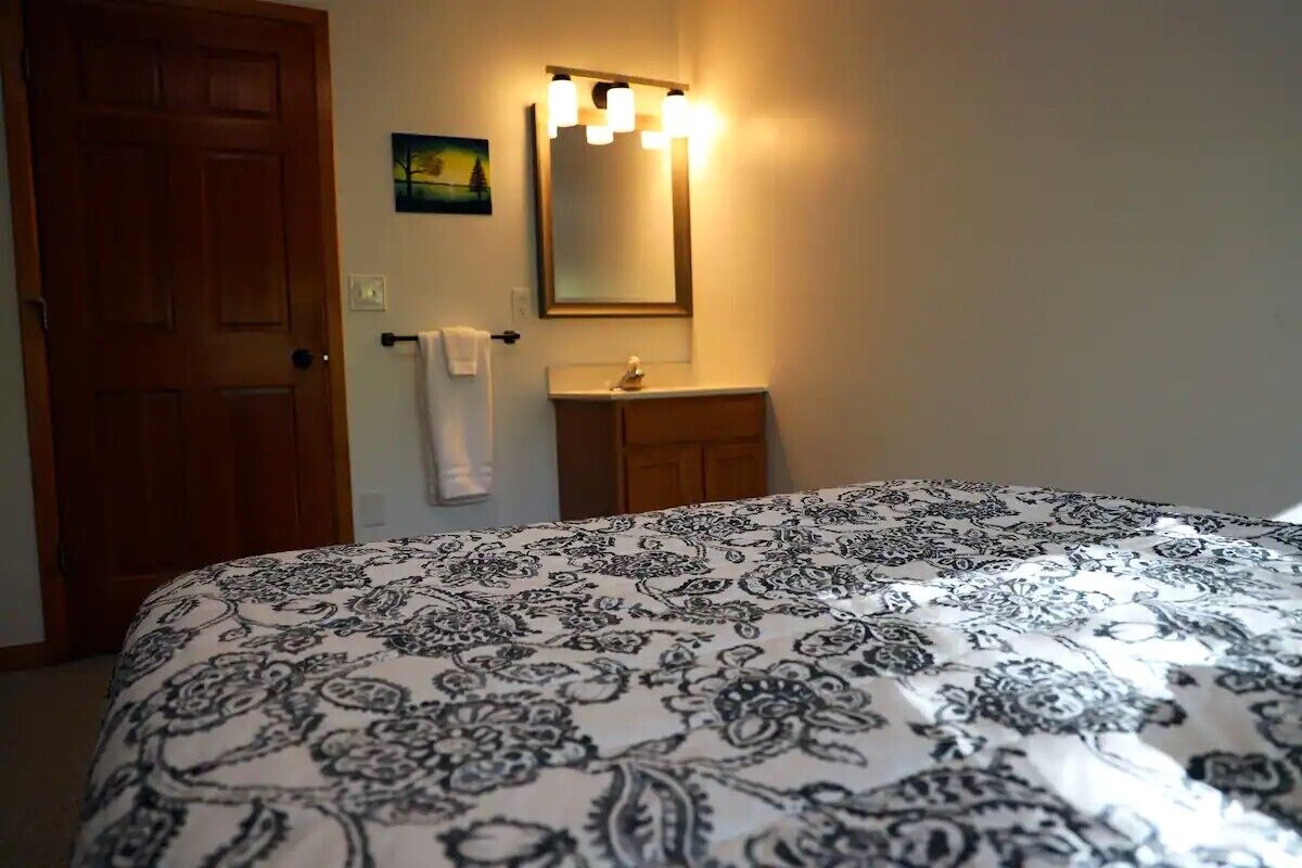 Un dormitorio con cama, una puerta de madera, un baño con lavabo y espejo, y una toalla colgada en la puerta.