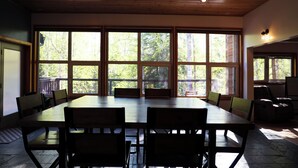 A dining area with a large table and chairs, large windows with a view of trees, and a wooden ceiling. - Spacious, Inviting, and Beautiful 4 Bedroom Home (Fairbanks)