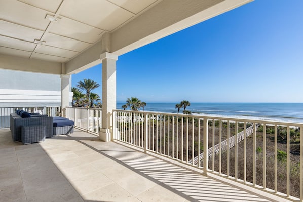 A covered balcony with outdoor furniture, a railing, and a view of the ocean.