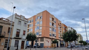 A multi-story residential building with balconies, a pedestrian crossing, and parked cars. - 114m² 3 Bedroom Apartment With Balcony Lift and AC (Nules)