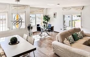 A spacious living area with a glass dining table, a sofa, and a fan.