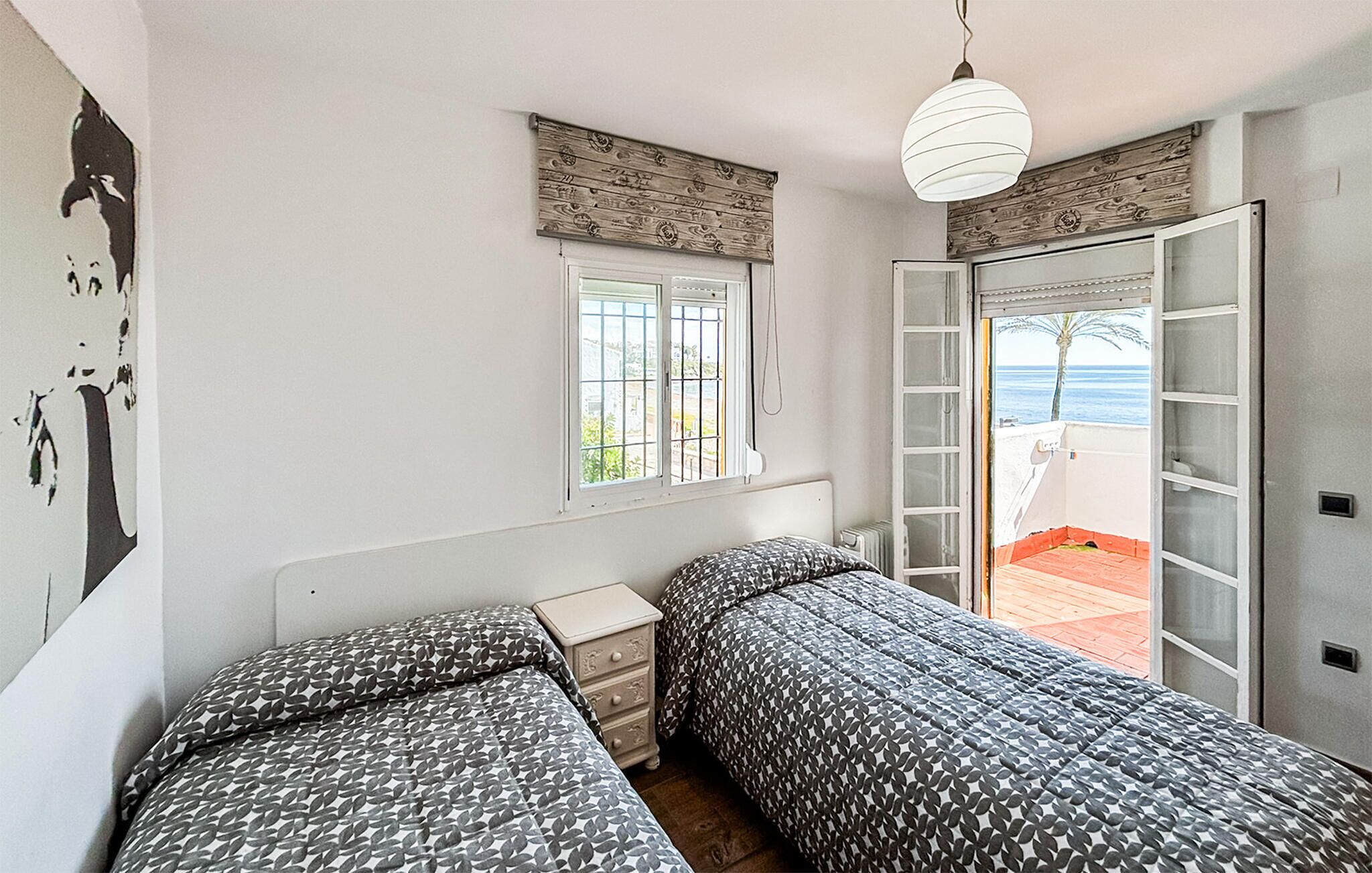 Un dormitorio con dos camas, una ventana, una puerta que da a un balcón y una lámpara fijada a la pared.