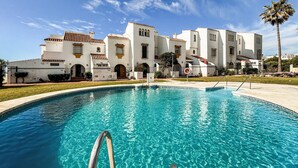 Une piscine à l’eau d’un bleu cristallin, entourée d’un bâtiment blanc doté de fenêtres en arc de cercle et d’un toit recouvert de tuiles.