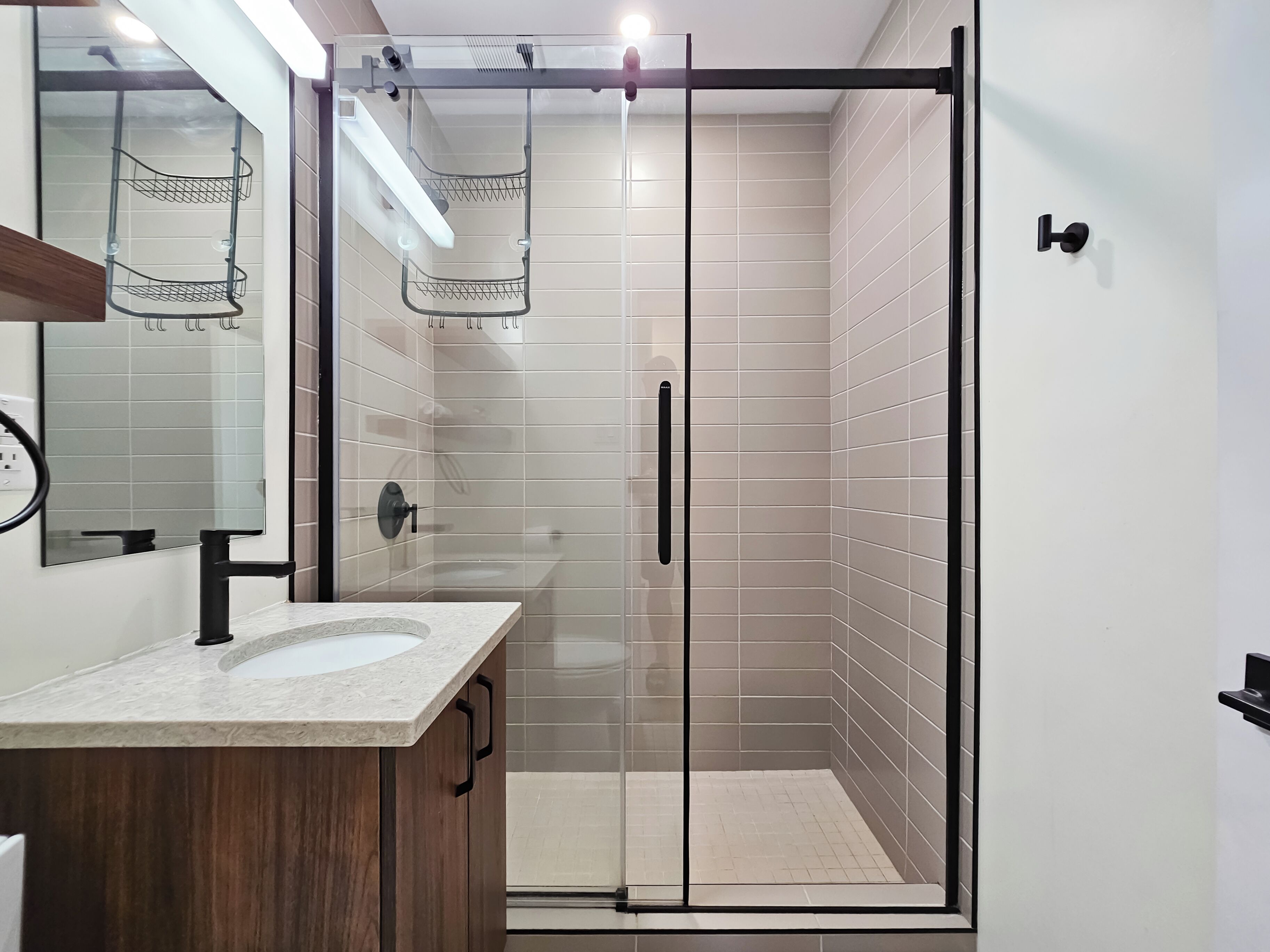 A modern bathroom with a glass-enclosed shower, a sink with a marble countertop, and a wooden cabinet.