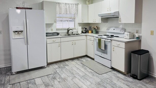 A modern kitchen with white cabinets, a refrigerator, a stove, and a trash bin. - Lumi House fully equipped house with everything you need for stay. (High Springs)