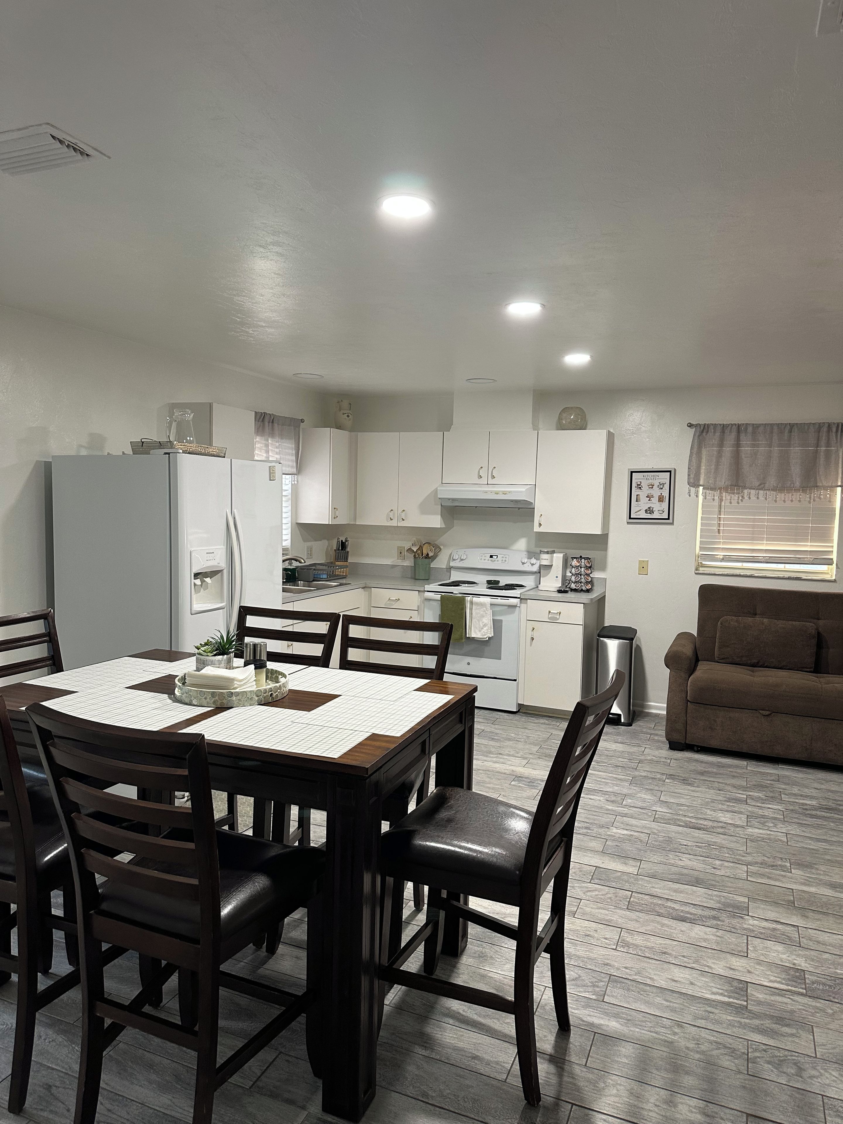 A compact kitchen with white cabinets, a dining table with chairs, and a brown sofa in a living area.
