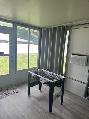 A room with a foosball table, a window with curtains, and a radiator.