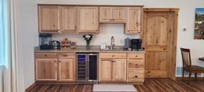 Eine Küche mit Holzausstattung, einer Kaffeemaschine, einem Kühlschrank und einem Essbereich mit einem Stuhl.