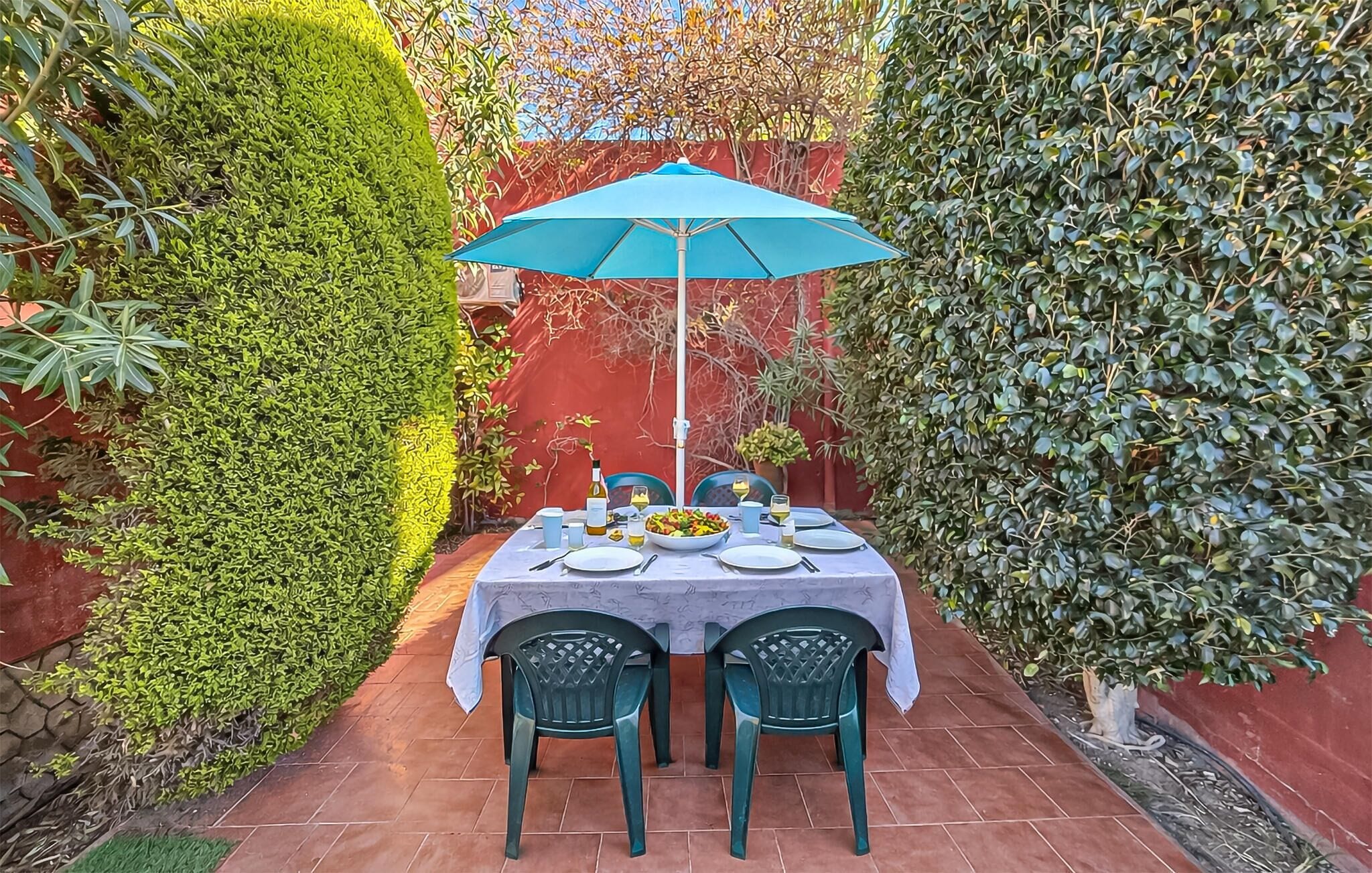 Een tafel gedekt voor twee met een blauwe parasol, omringd door groen en een rode muur.