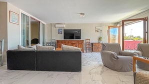 Un salon avec un canapé, des fauteuils, un téléviseur et un balcon.