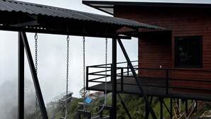 Una cabaña de madera con un columpio y vista a un paisaje brumoso.