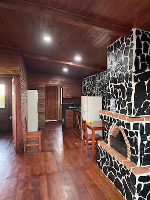 Um interior rústico com lareira de pedra, piso de madeira e área de cozinha.