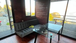 Una habitación moderna con una mesa de vidrio, un sofá gris y ventanas amplias.