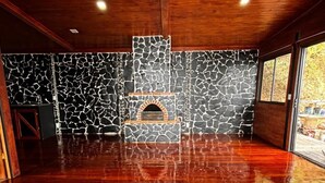 Una habitación amplia con piso de madera, una pared de piedra con chimenea y ventanas grandes.