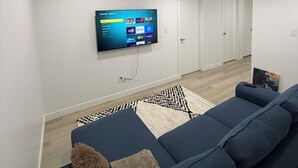 En moderne stue med et stort fladskærms-tv på væggen, en blå sofa, et mønstret tæppe og trægulv.