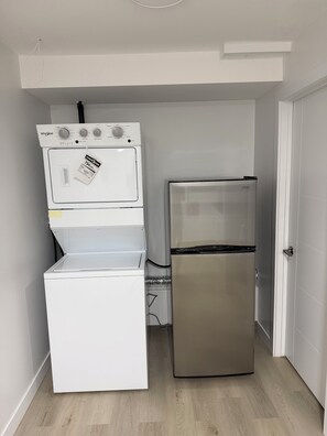 Eine kompakte Küche mit einer weißen Waschmaschine und einem Trockner, einem Edelstahlkühlschrank und Holzboden.