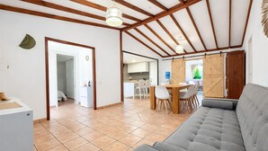 Ein großzügiger Wohnbereich mit einer Couch, Esstisch und Stühlen, einer Küche im Hintergrund und einer Holzbalkendecke.