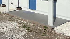 A white building with a blue door, a small porch, and a tree in the background. - Blue Tide Retreat, Walk to Beach, Perfect for Long Term Stays! (Madeira Beach)
