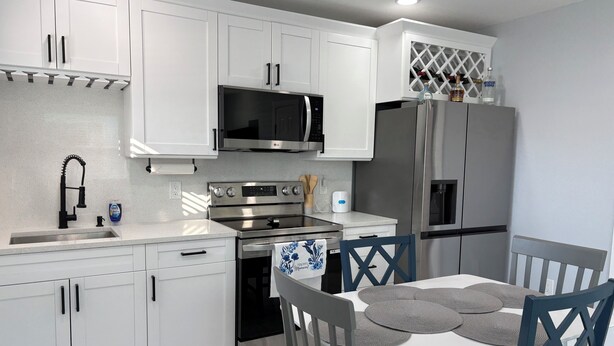 A modern kitchen with white cabinets, stainless steel appliances, and a dining area with a table and chairs. - Blue Tide Retreat, Walk to Beach, Perfect for Long Term Stays! (Madeira Beach)