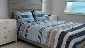 A bedroom with a bed, nightstands, a ceiling fan, and windows. - Blue Tide Retreat, Walk to Beach, Perfect for Long Term Stays! (Madeira Beach)