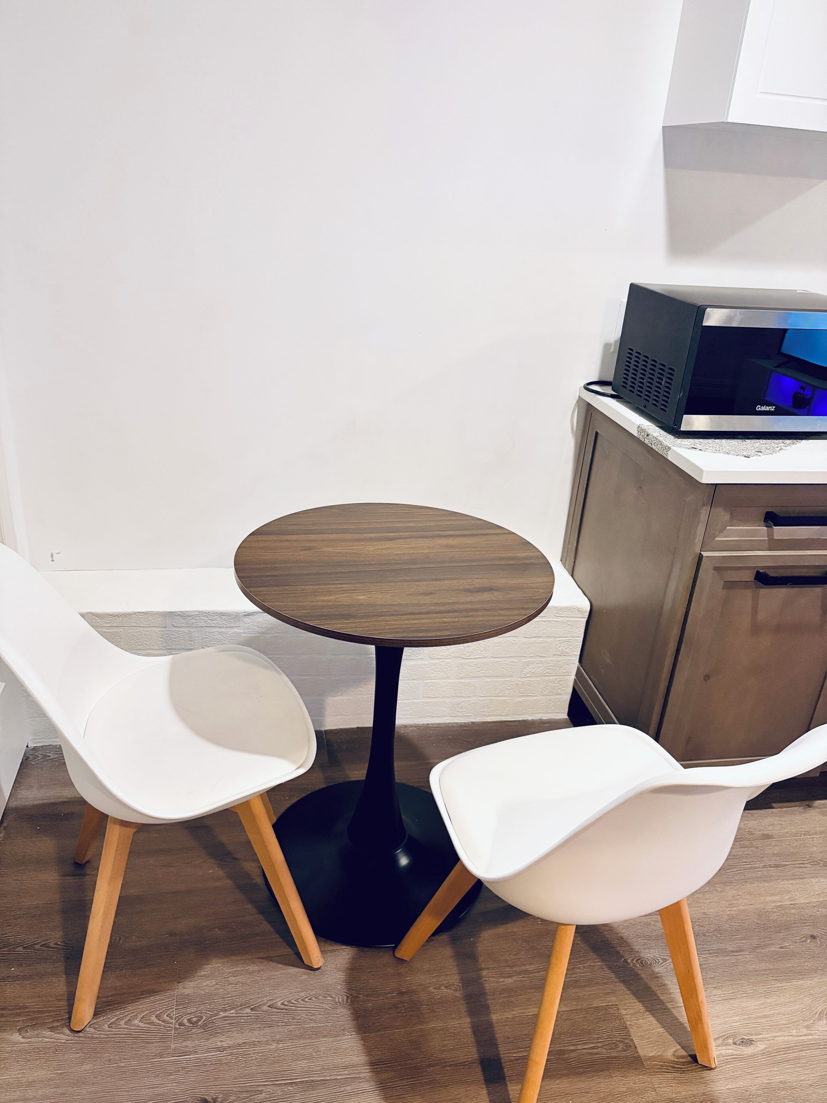 A small round table with two white chairs, a microwave, and a wooden cabinet.