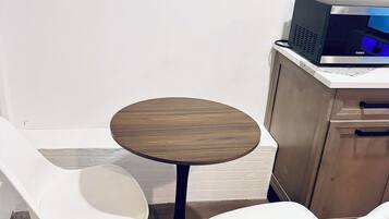 A small round table with two white chairs, a microwave, and a wooden cabinet.