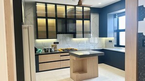 A modern kitchen with a central island, dark cabinetry, and a marble backsplash.