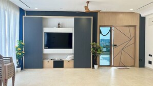 A modern living room with a large flat-screen TV, a sliding glass door, and a potted plant.